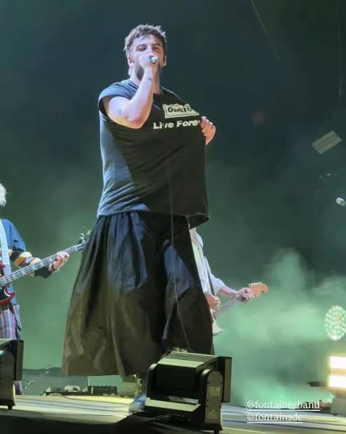 Grian Chatten canta con Fontaines D.C. y muestra una camiseta de Oasis con la frase Live Forever